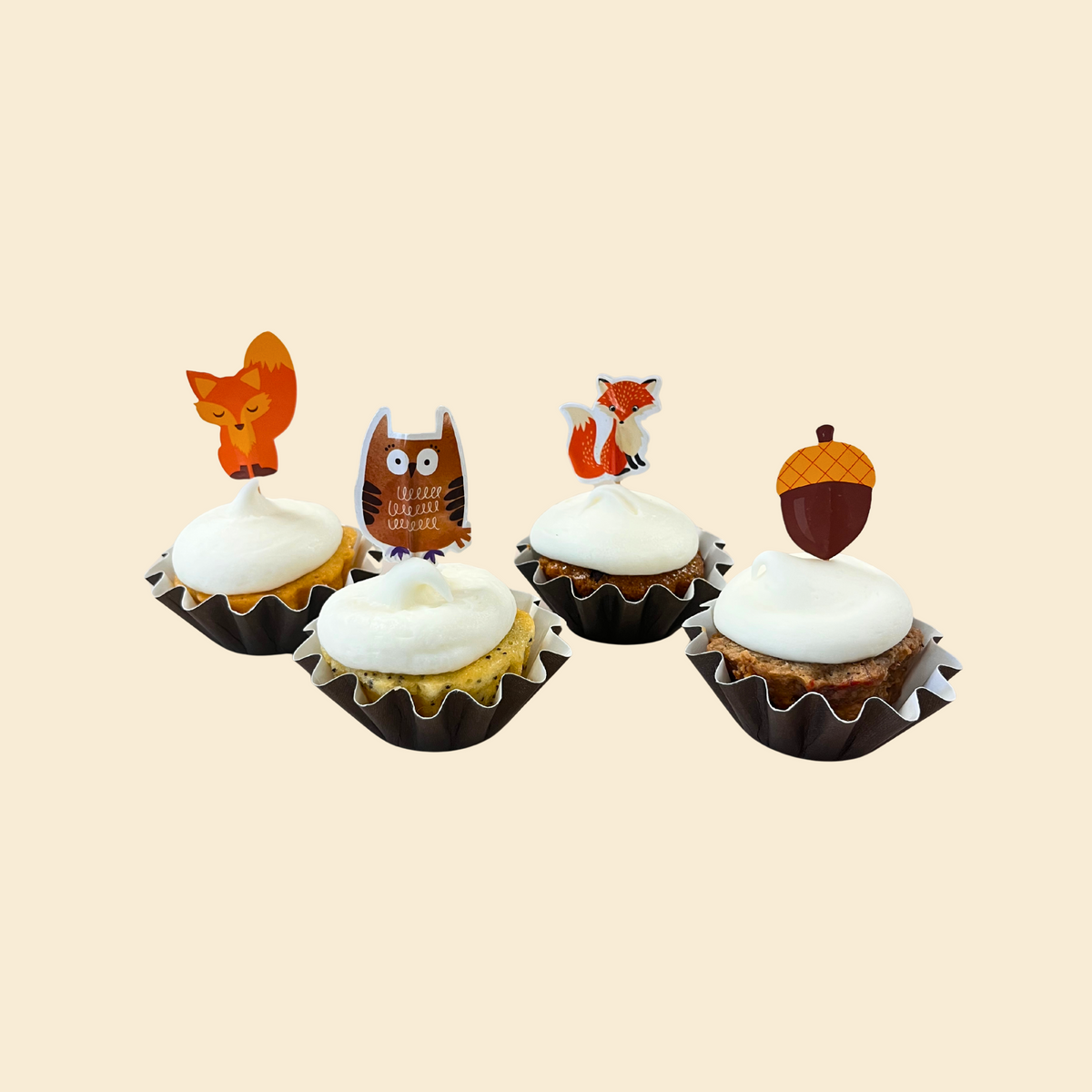 Four cupcakes with fall animal-themed toppers on a beige background