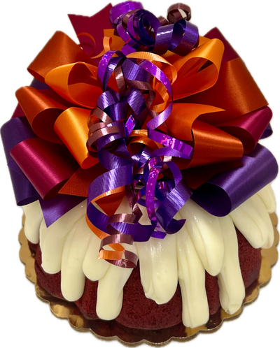 A cake decorated with a handcrafted bow featuring festive fall colors, in this case, purple and orange, on a red velvet Bundt cake.